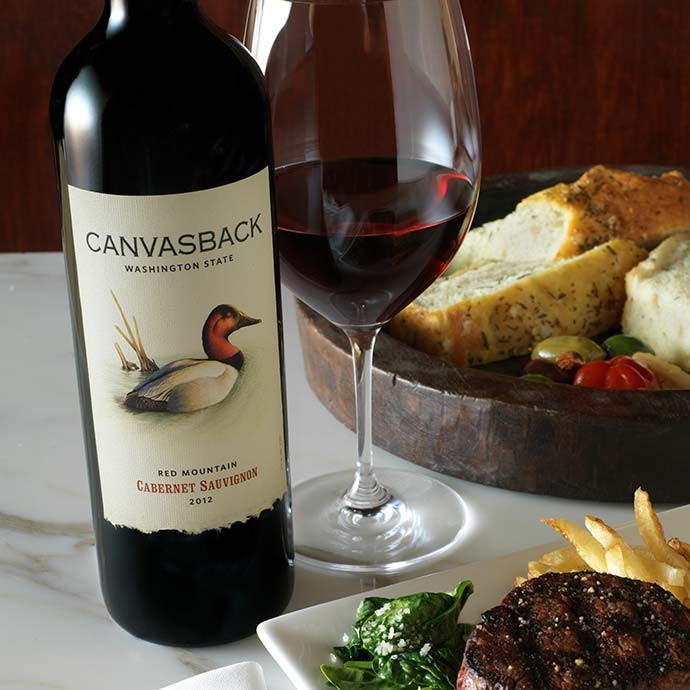 Bottle of Canvasback on table with glass and plate of food