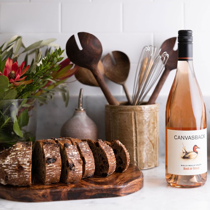 A bottle of Canvasback wine next to a plate of sliced bread and flowers.